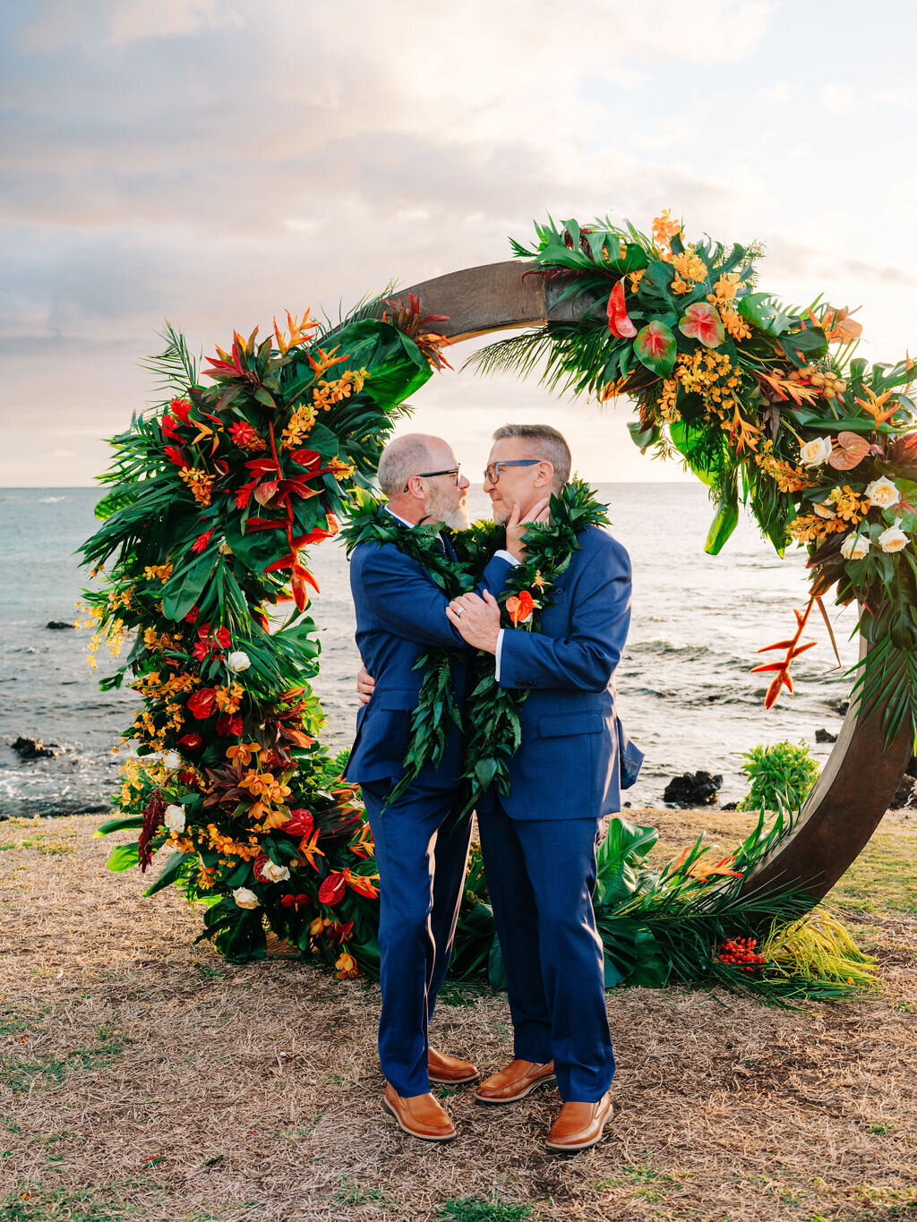 Kailua Kona Wedding PlannerLGBTQ+ wedding with two grooms exchanging vows under a round wood arch adorned with bright tropical florals at the Fairmont Orchid in Hawaii.