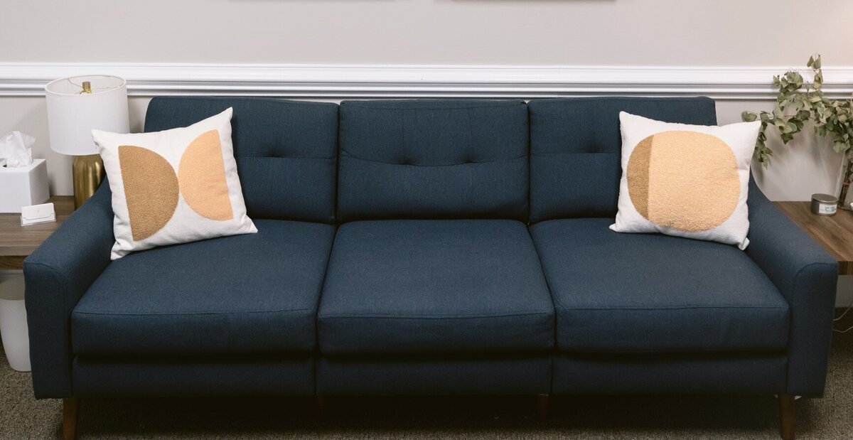 Blue coach in a therapist office with two white pillows that have an orange pattern on them