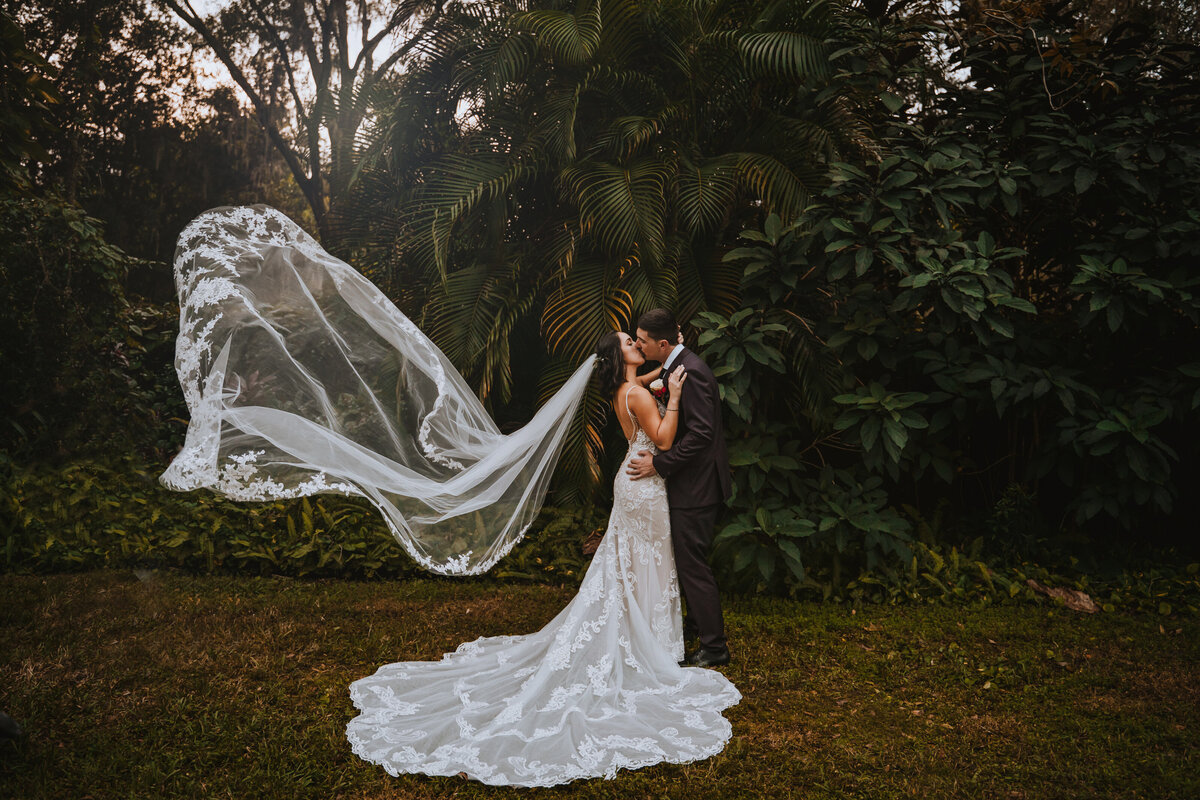 bride and groom kissing with veil flying in the wind
