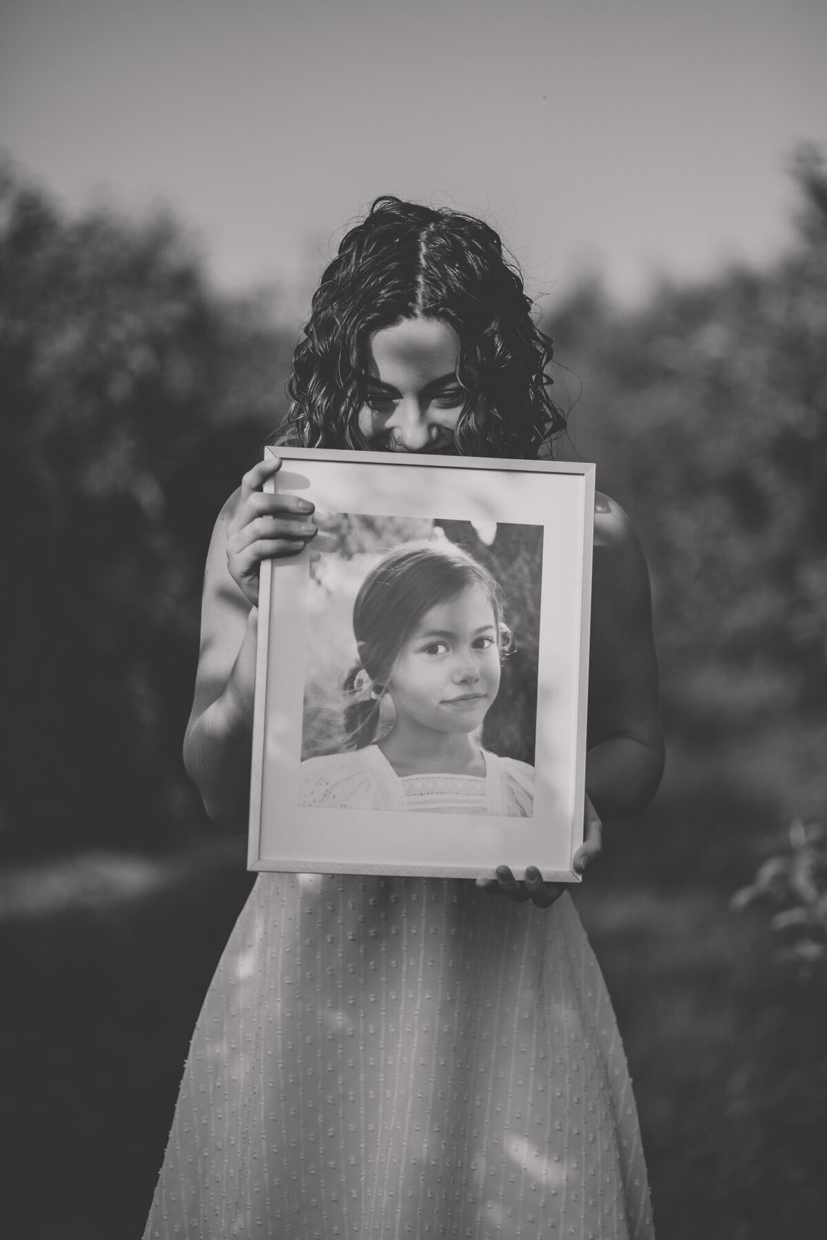 Black and white image of female in white dress holding a school age image of herself