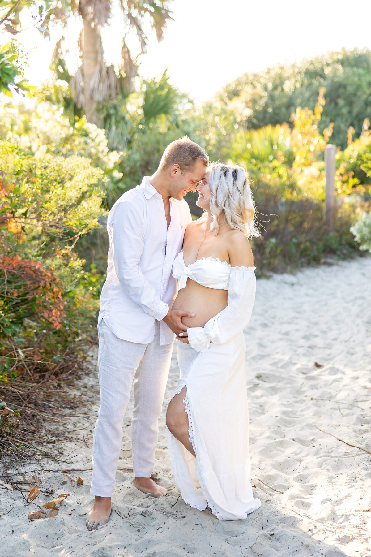 Man holding his pregnant partners belly outside on a beach