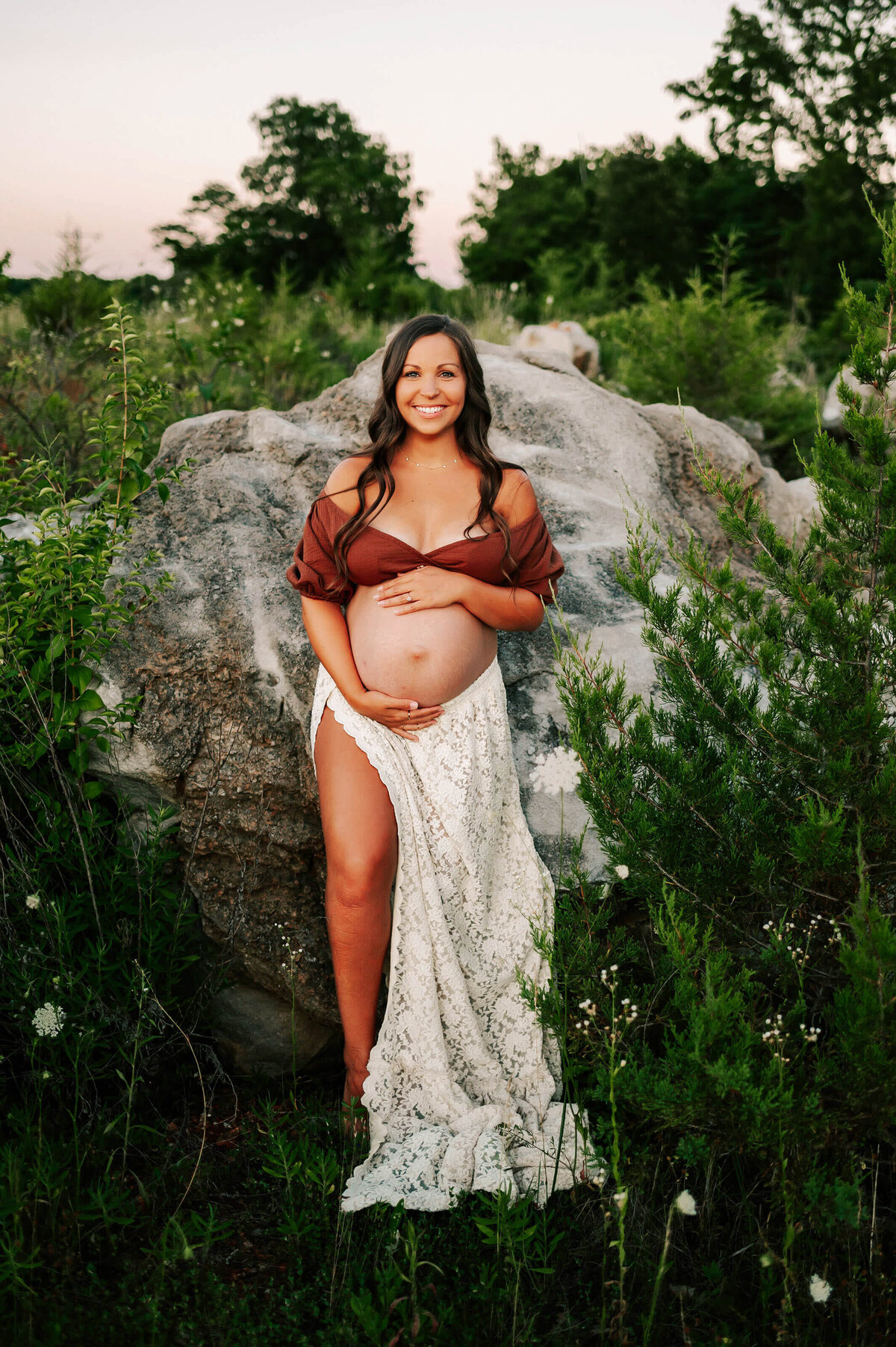 maternity photo of mom leaning against rock outdoors holding baby bump in Joplin MO