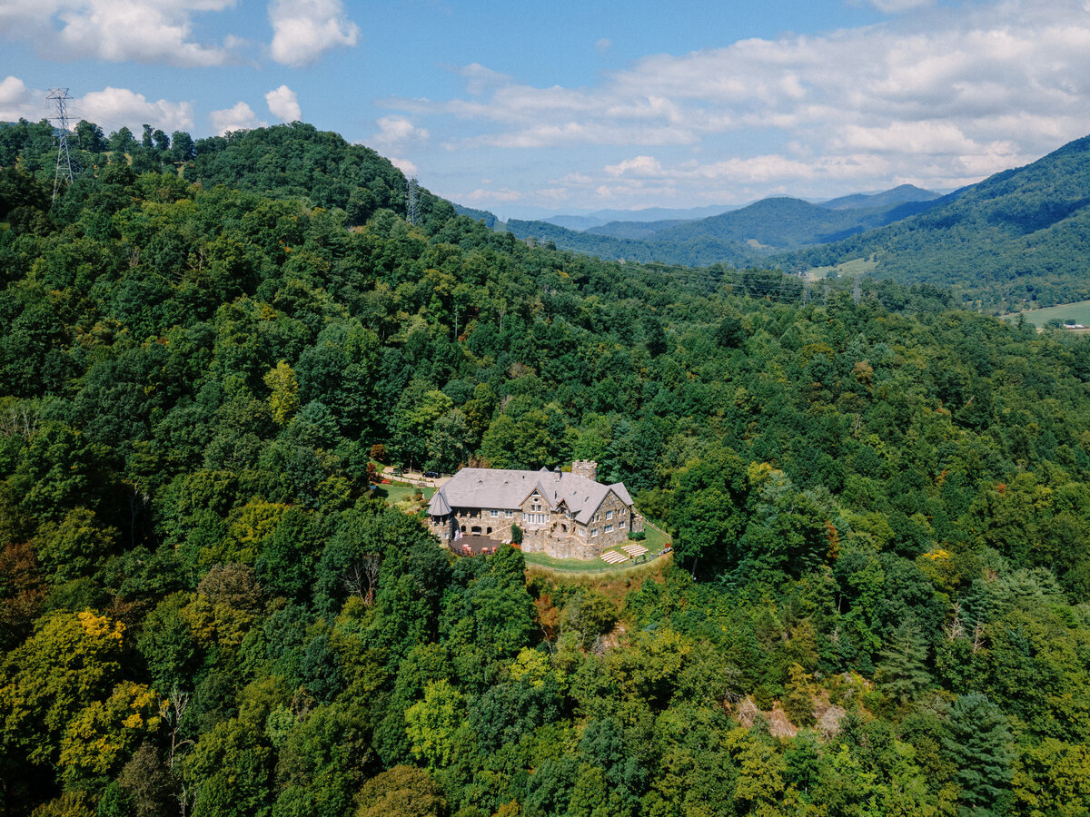 Aerial drone view of Castle Ladyhawke surrounded by lush mountain scenery in Tuckaseegee, North Carolina—an iconic mountaintop wedding venue.