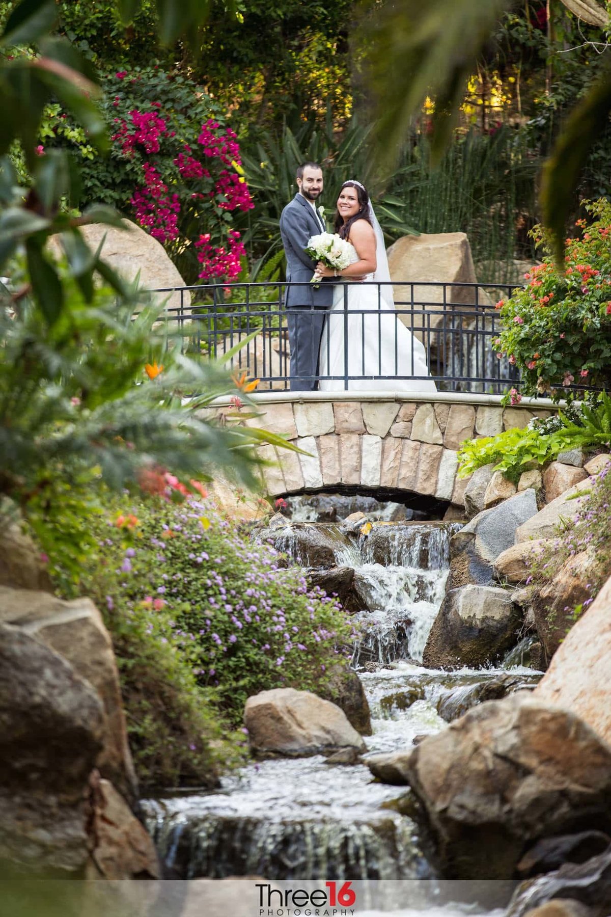Bride and Groom pose together on a bridge overlooking an amazing waterfall and rock scenery