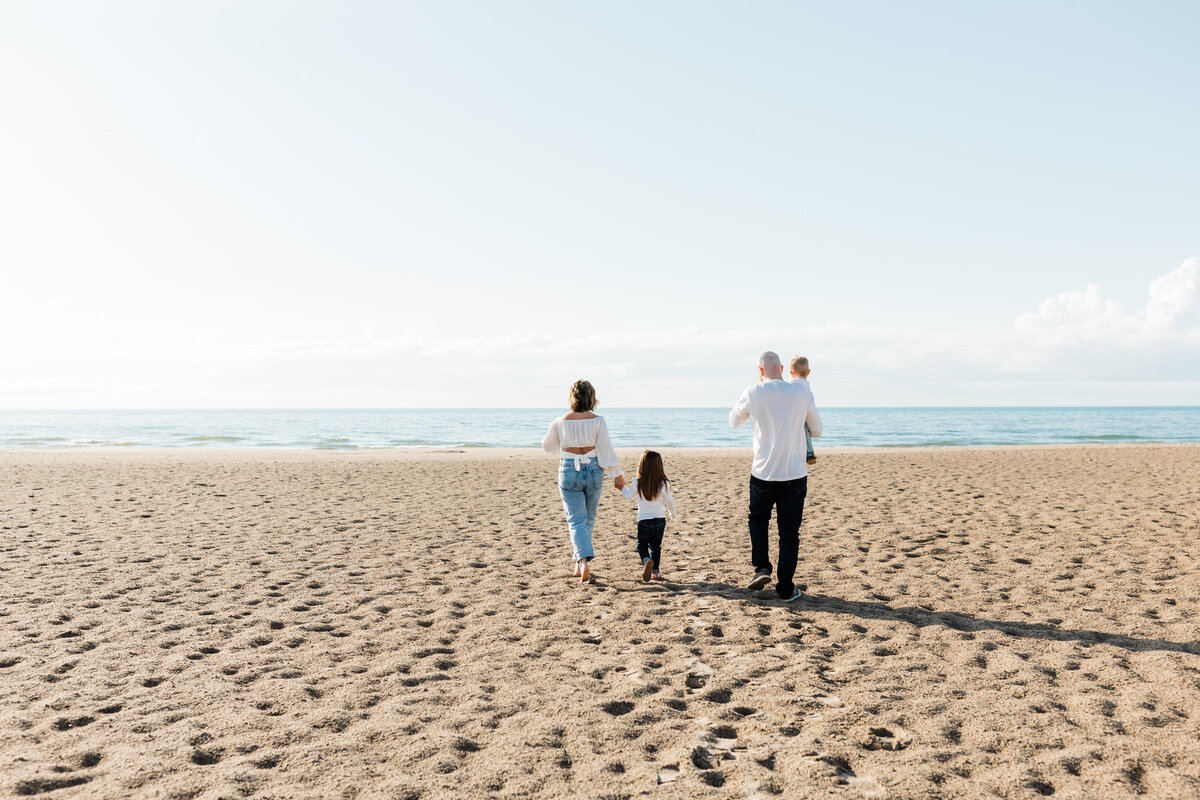 Family walking hand-in-hand along a sandy beach during a lifestyle photo session near South Bend.