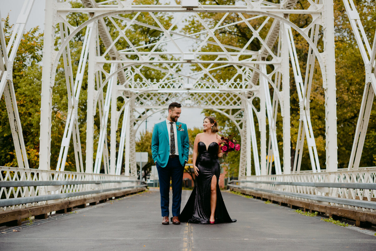 bride wearing a black sequenced dress and groom wearing a turquoise suit on white bridge