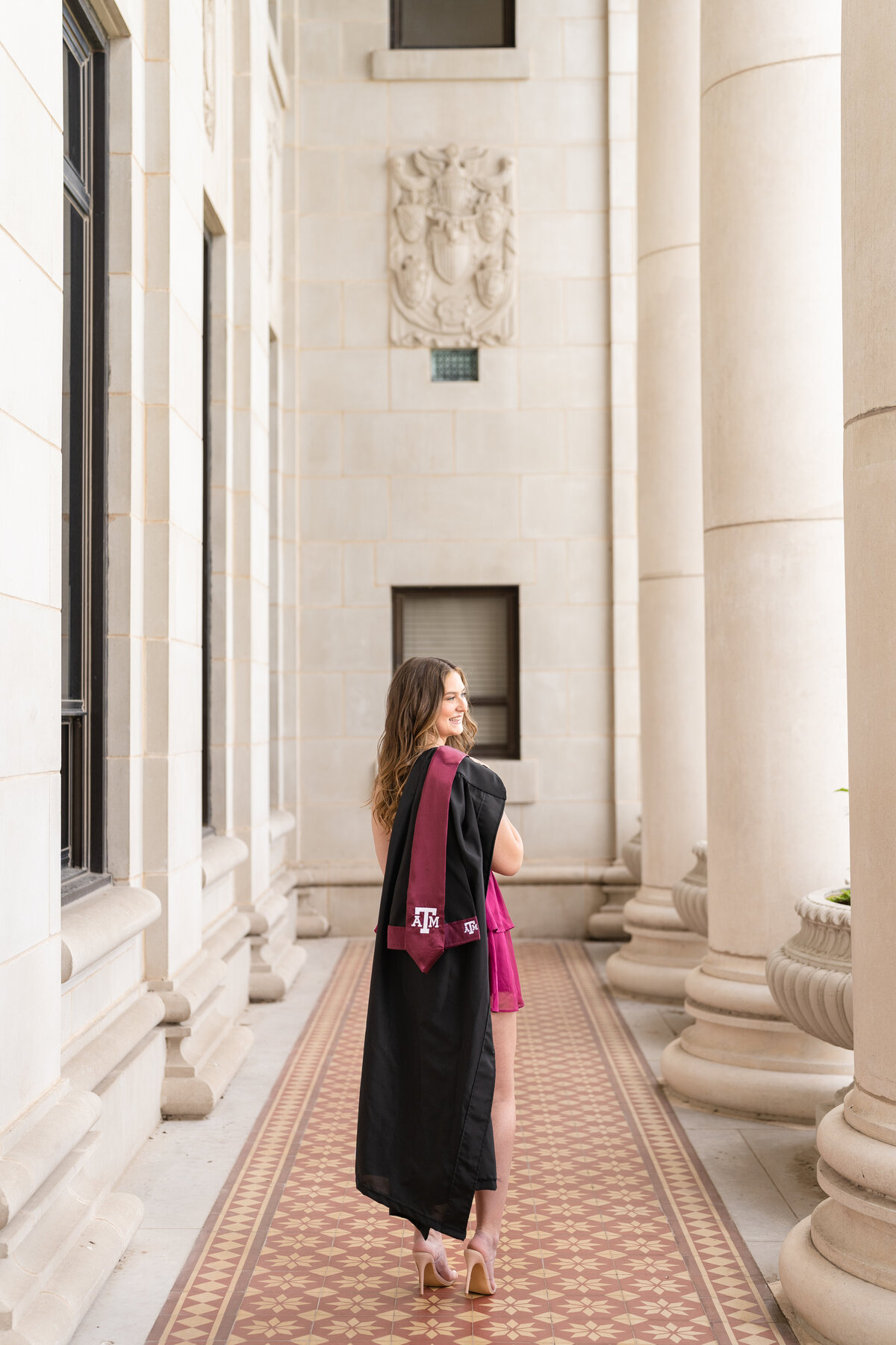 Texas A&M senior girl holding gown and stole over shoulder and looking away in the columns of the Administration Building