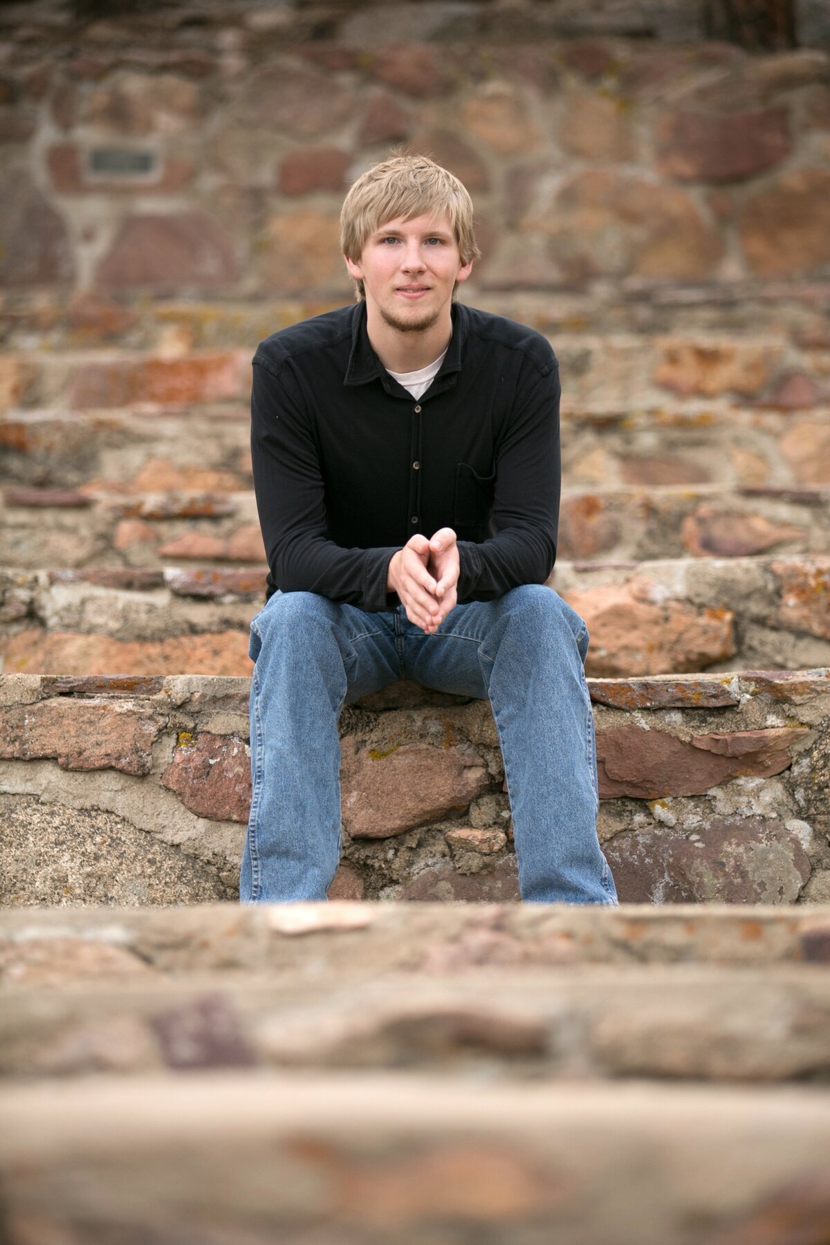 a young man sits on rock steps for a senior portrait