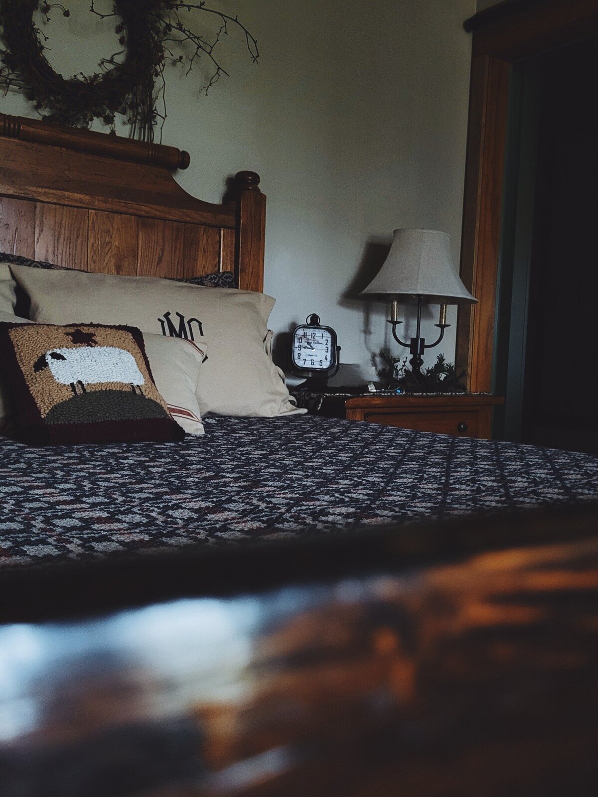 Oak bed and nightstand with early American textiles and monogrammed pillows dark and moody with deep blues
