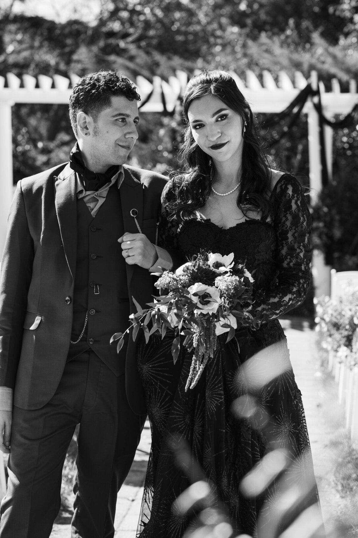 Black and white picture of young couple of bride. holding her bouquet and wearing a black dress.