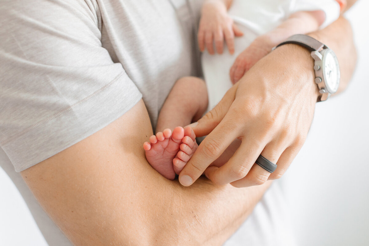 close up image of dad holding newborn baby's toes