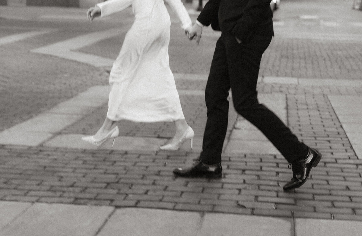 Black and white photo of a couple walking hand in hand through downtown Indianapolis near Bottleworks Hotel and Monument Circle, captured by Rainstorm Photo & Video in a candid, documentary style.