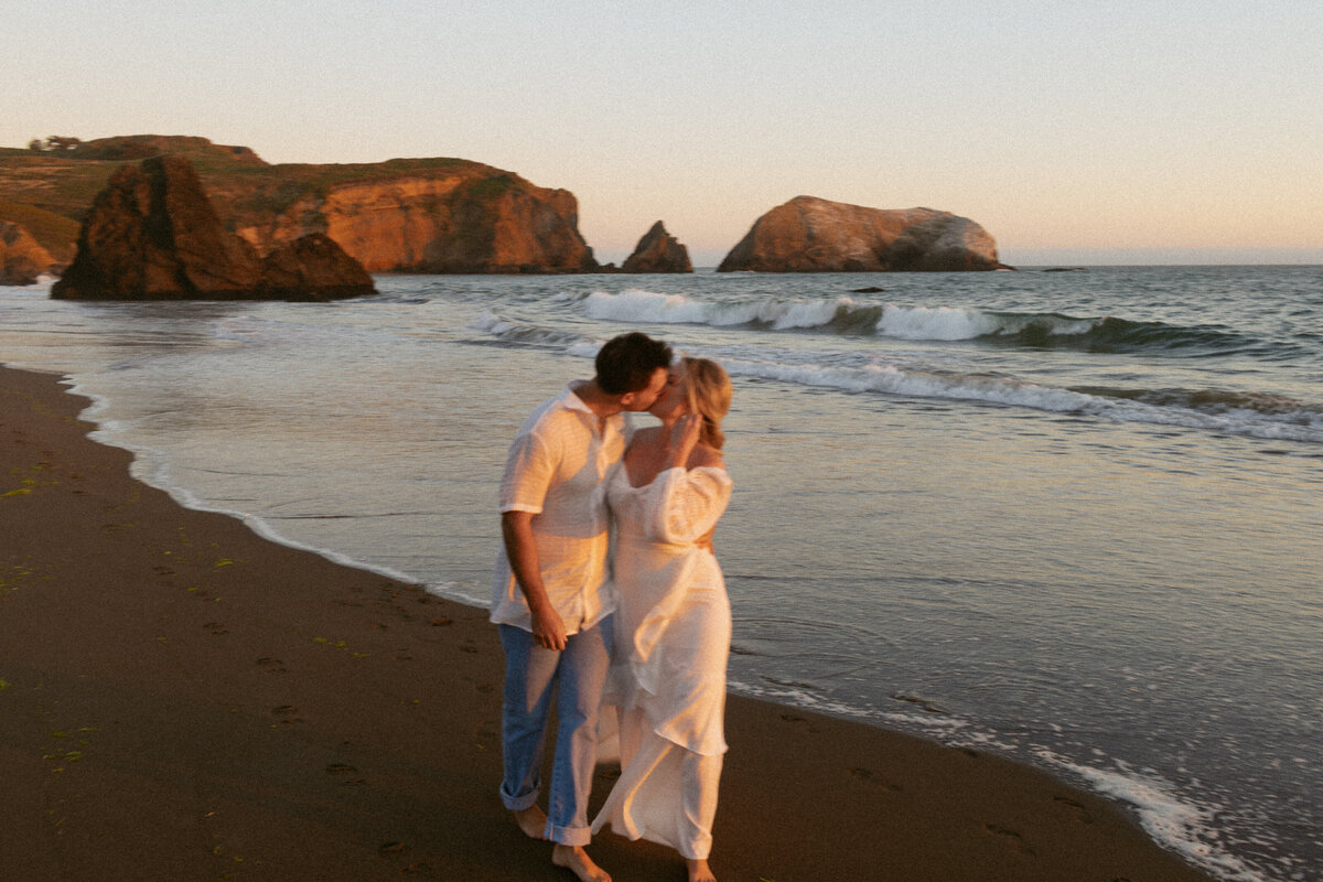 A couple enjoying a romantic moment on the beach at sunset in California, with the golden hues reflecting on the water.