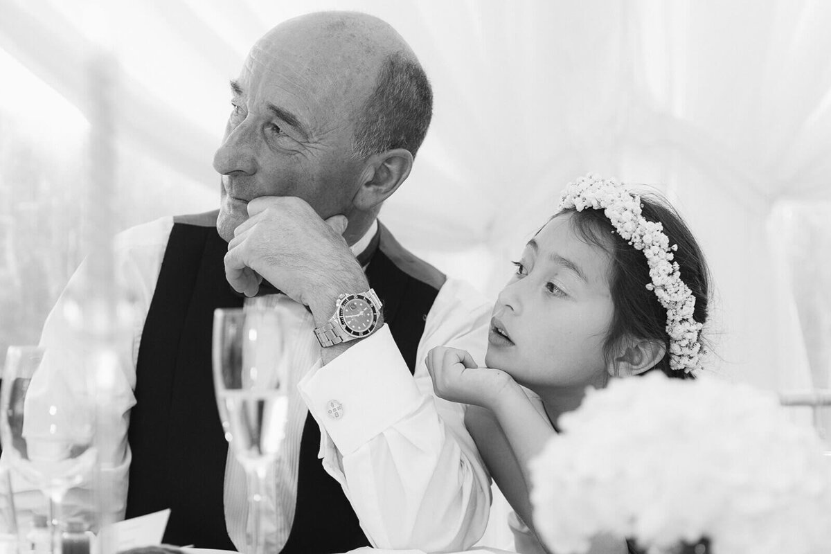 A grandad and young granddaughter gaze at the bride at the wedding top table