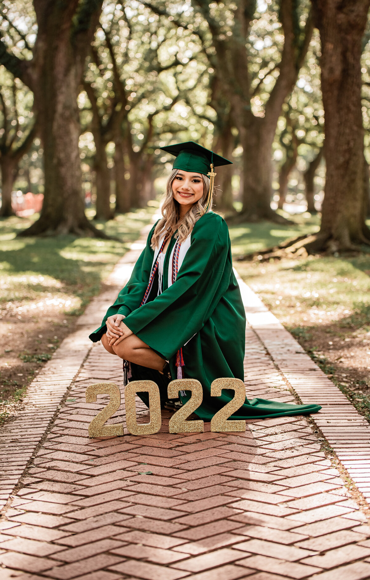 A graduate squats in front of a "2022" sign while wearing her cap and gown.
