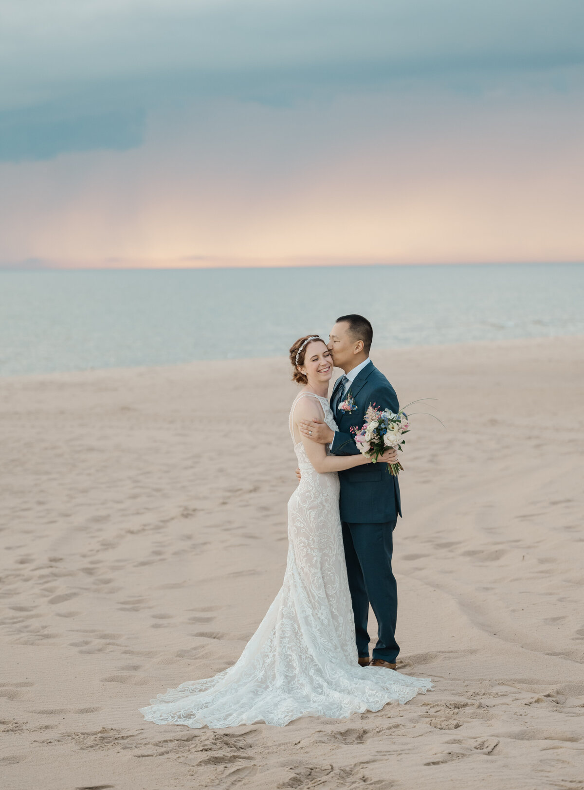 A bride and groom walk along the beach by Lake Michigan at sunset