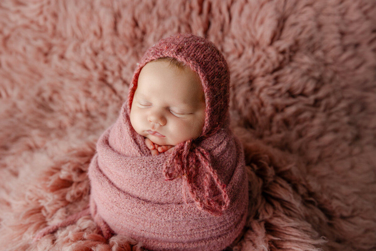 Baby girl sleeping soundly in a warm pink setup with coordinating knits and cozy textures. Photographed by Inland Empire newborn photographer Kaitlyn Dawn.