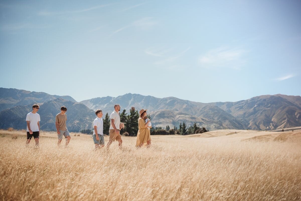 a family of 6 walking through the grass with the wanaka mountains in the background