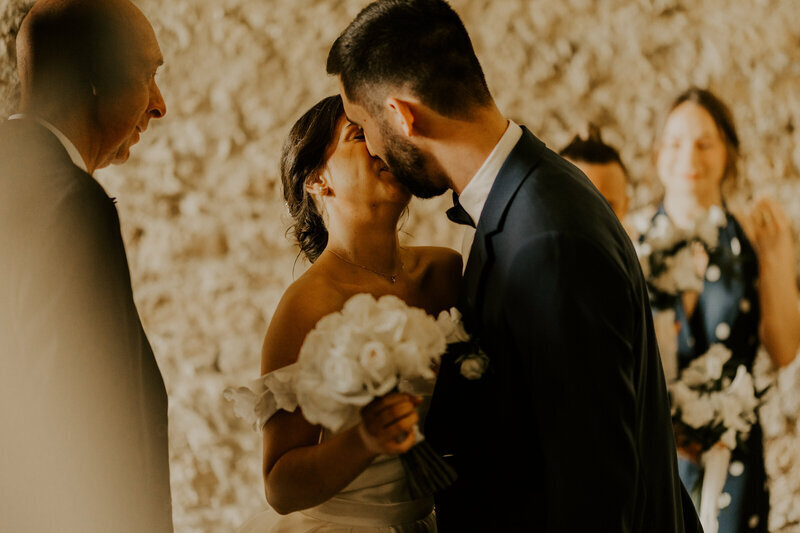 Mariés échangeant un baiser sous le regard de leurs invités. Photo immortalisée par Laura, photographe de mariage en Vendée.