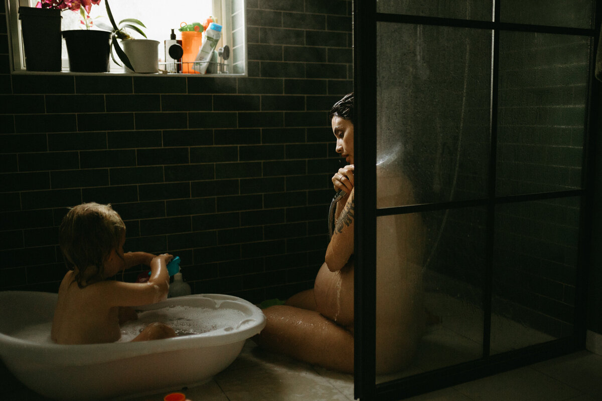 En gravid mamma tittar på när sonen och pappan till sonen leker tillsammans. Gravidfotografering Göteborg.