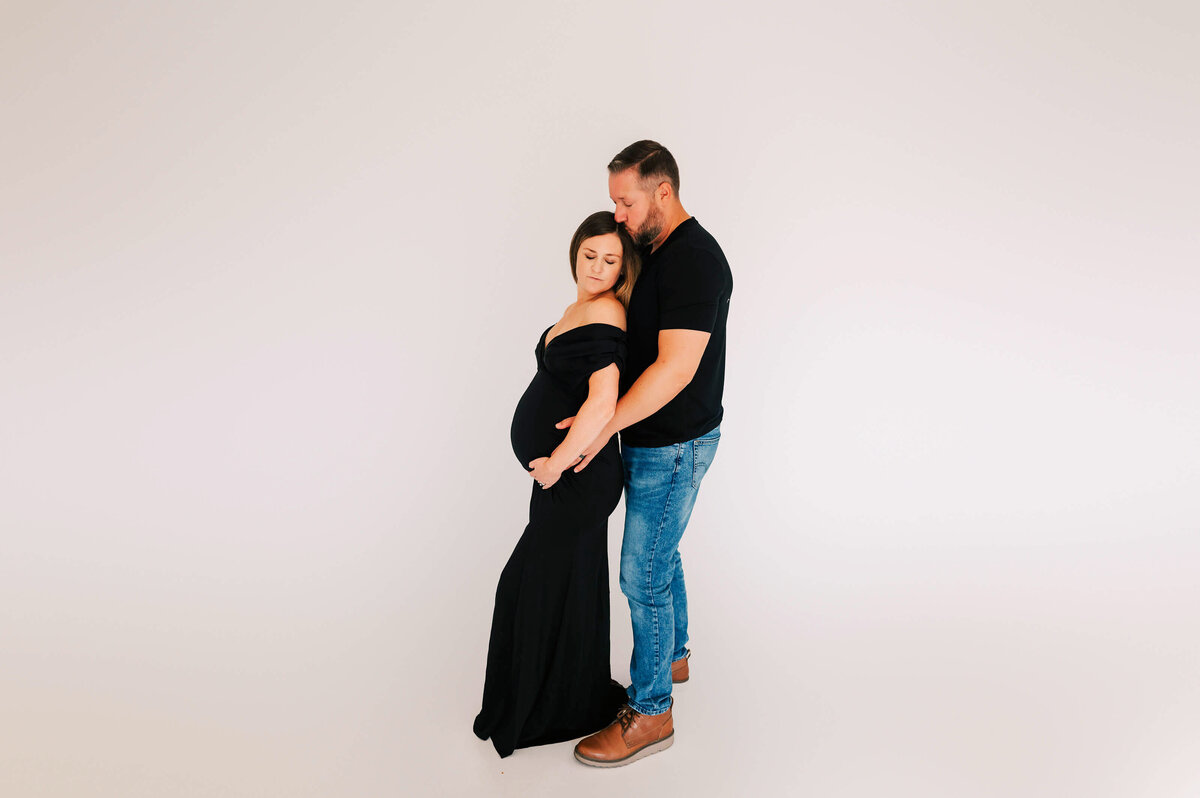 pregnant mom in black gown kissed by her husband during Springfield MO maternity photography sesssion