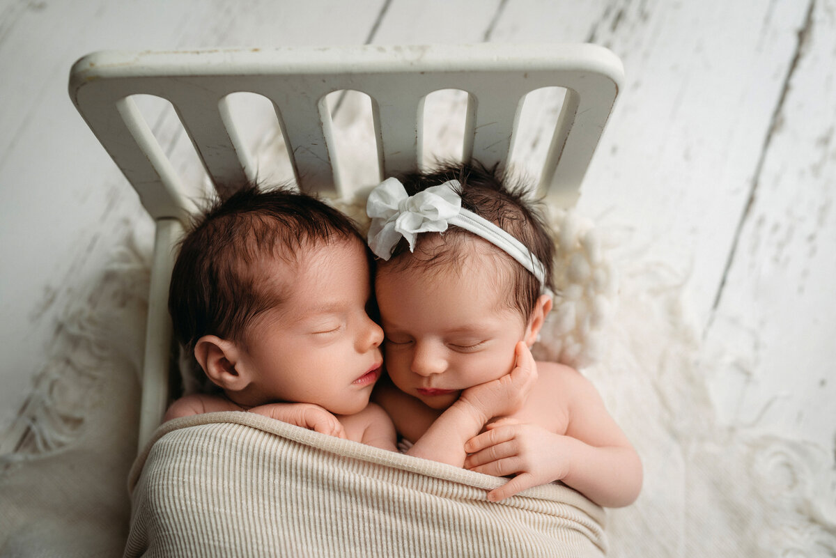 Twin newborns wrapped together in miniature white baby bed