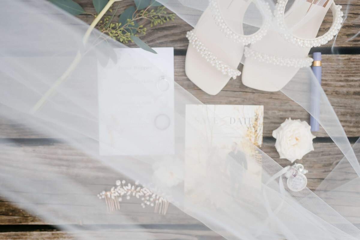 brides veil flows over a flatlay of bridal details laying over a wooden desk at Charlottesville wedding venues