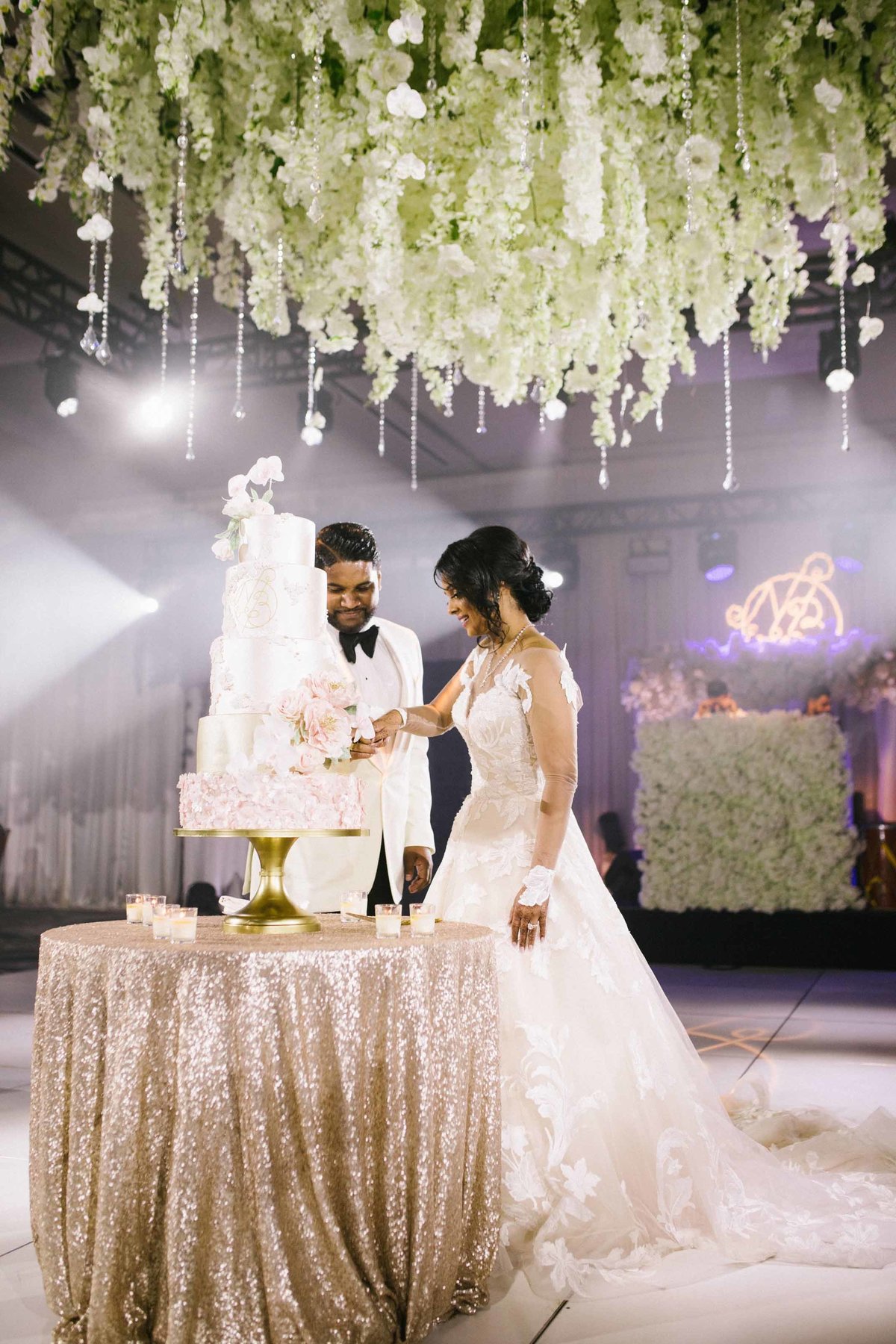 Beautiful Seattle couple cut their wedding cake under a huge white floral chandelier