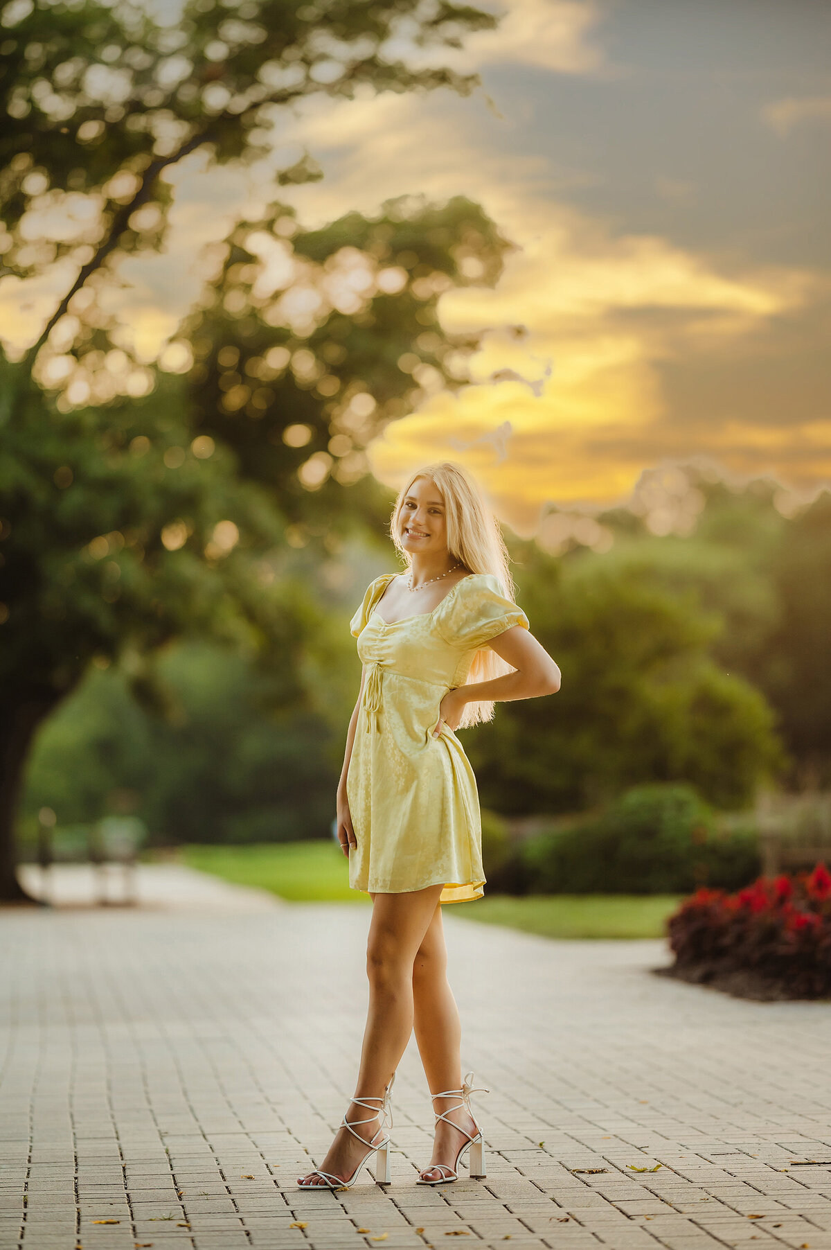 A girl from Brookfield Central High School stands on a brick path at Paradise Springs in Eagle while wearing a yellow sundress and white strappy heels for her senior photos.