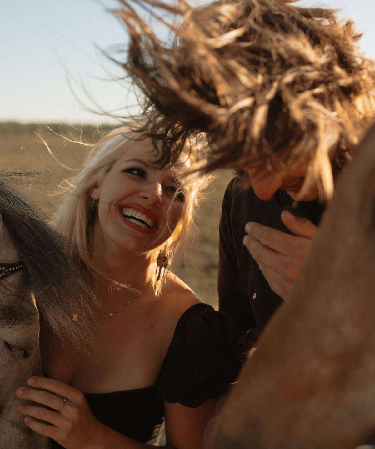 candid shot of couple laughing together at sunset with their horse at their side