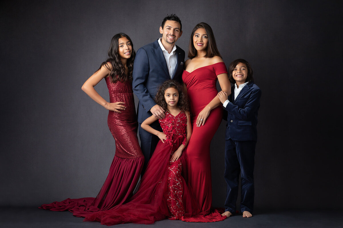 Dallas family photographer capturing a family in coordinating red and navy attire, featuring sequined dresses and velvet suits. The family poses together against a dark backdrop for a stylish and timeless family portrait.