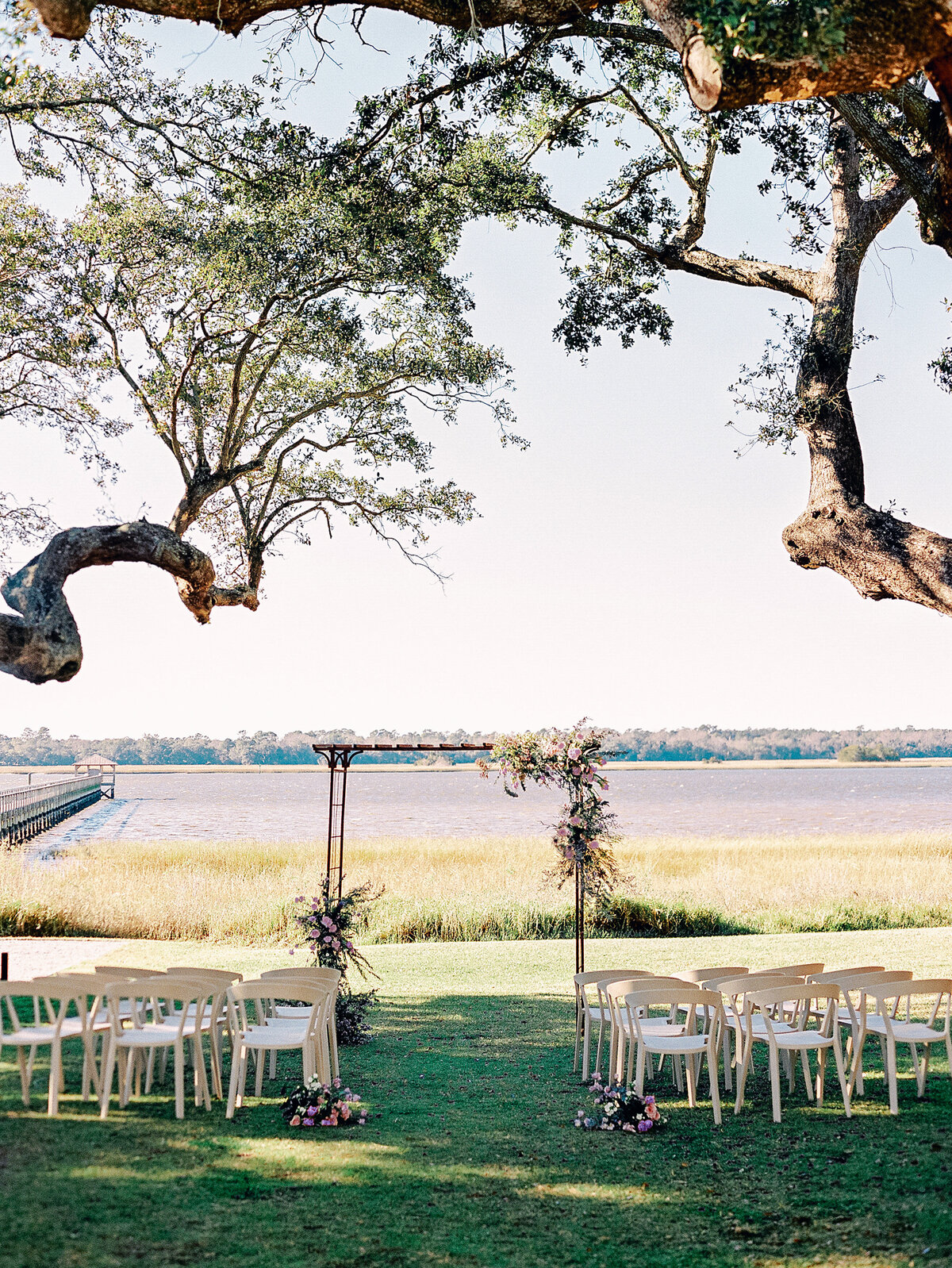 Floral arch at wedding ceremony with chairs in front of river in Charleston