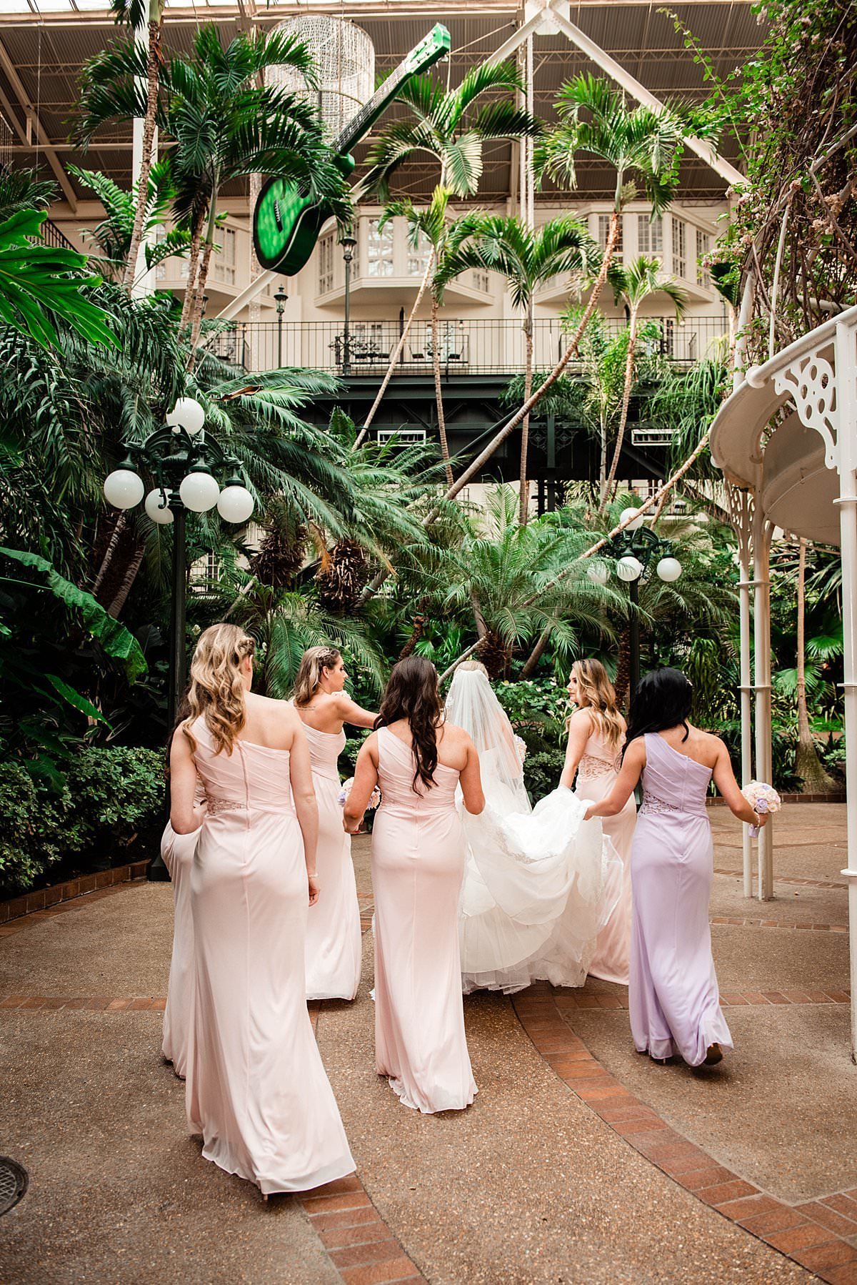 Bridesmaids helping carry brides train through the tropical plants inside of Gaylord Opryland