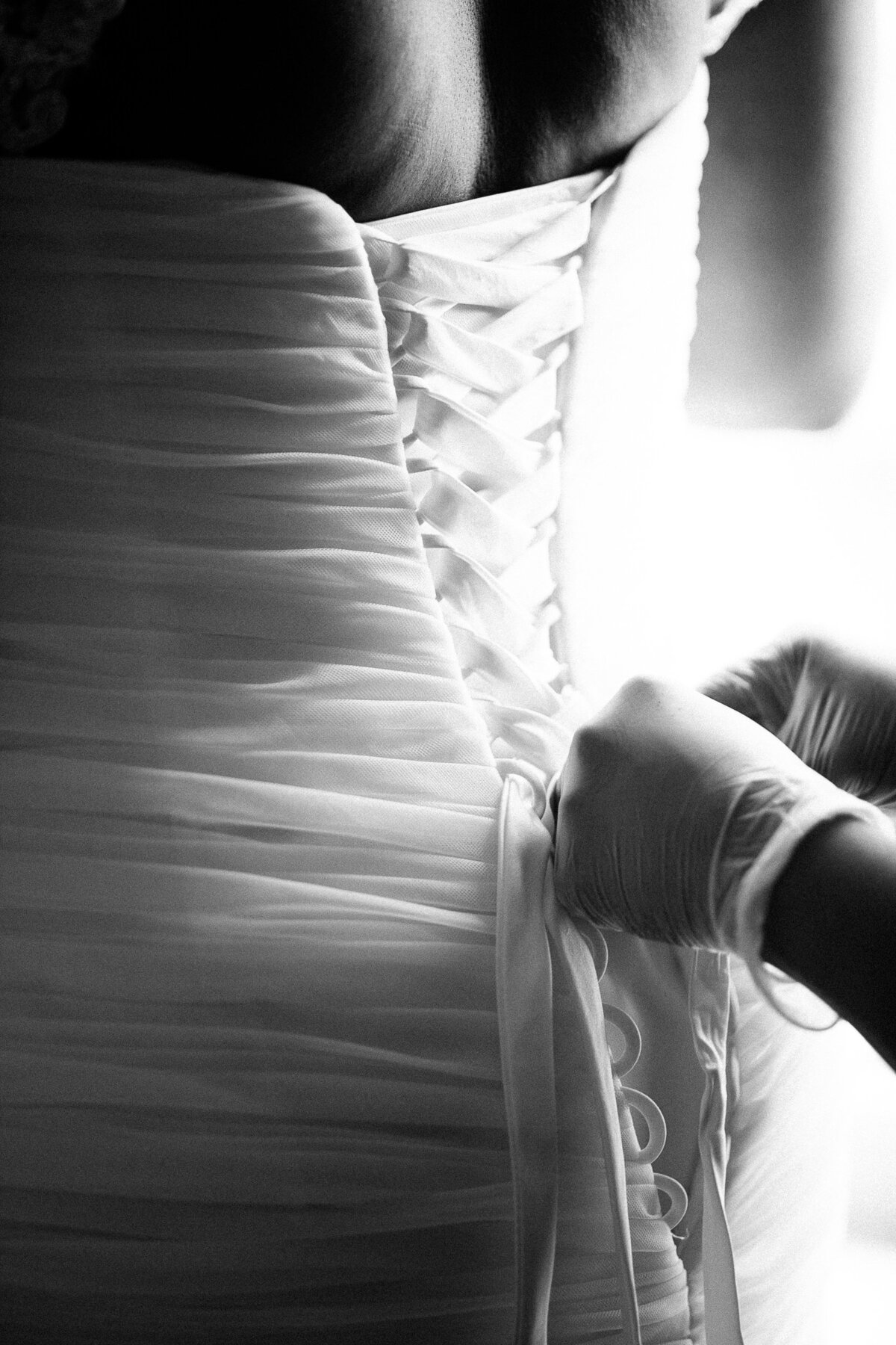 A bridesmaids wears gloves while lacing up the back of the wedding dress, so she doesn’t make any marks on the white material.