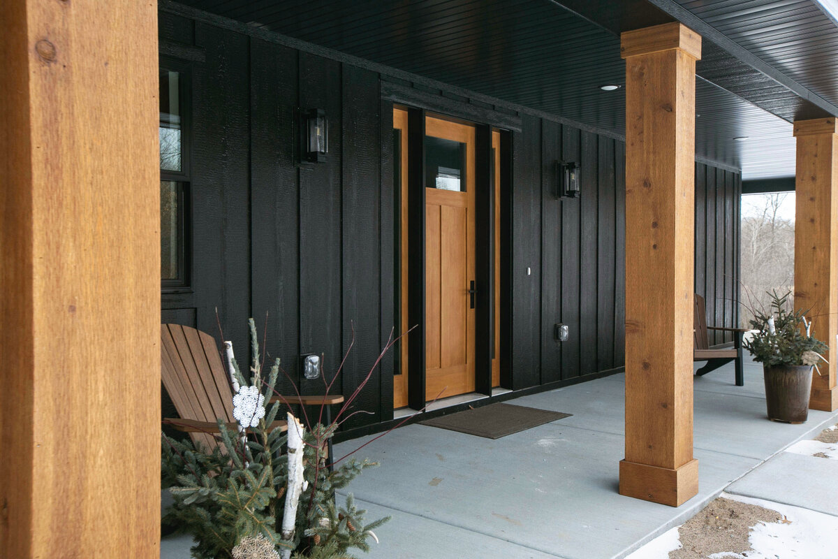 Exterior view of custom home in Elk River, Minnesota with black siding, wood details and front porch built by Cornerstone Custom Builds