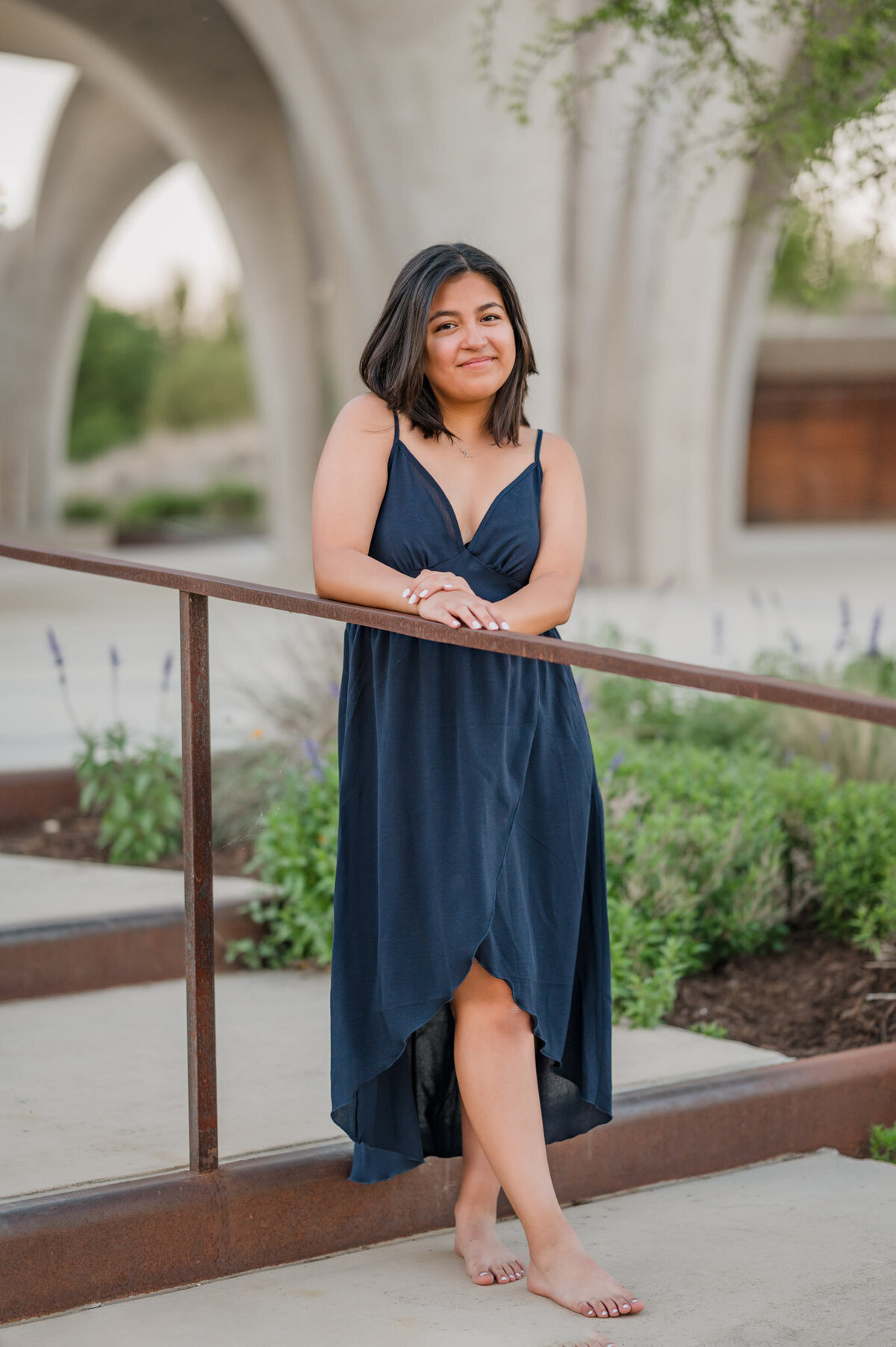 Girl in a blue dress leans on a stair rail and smiles at San Antonio Senior Photographer Cassey Golden.