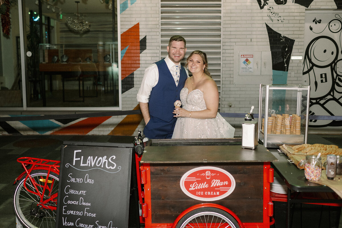Bride and groom pose with the Little Man Ice Cream cart at their wedding reception.