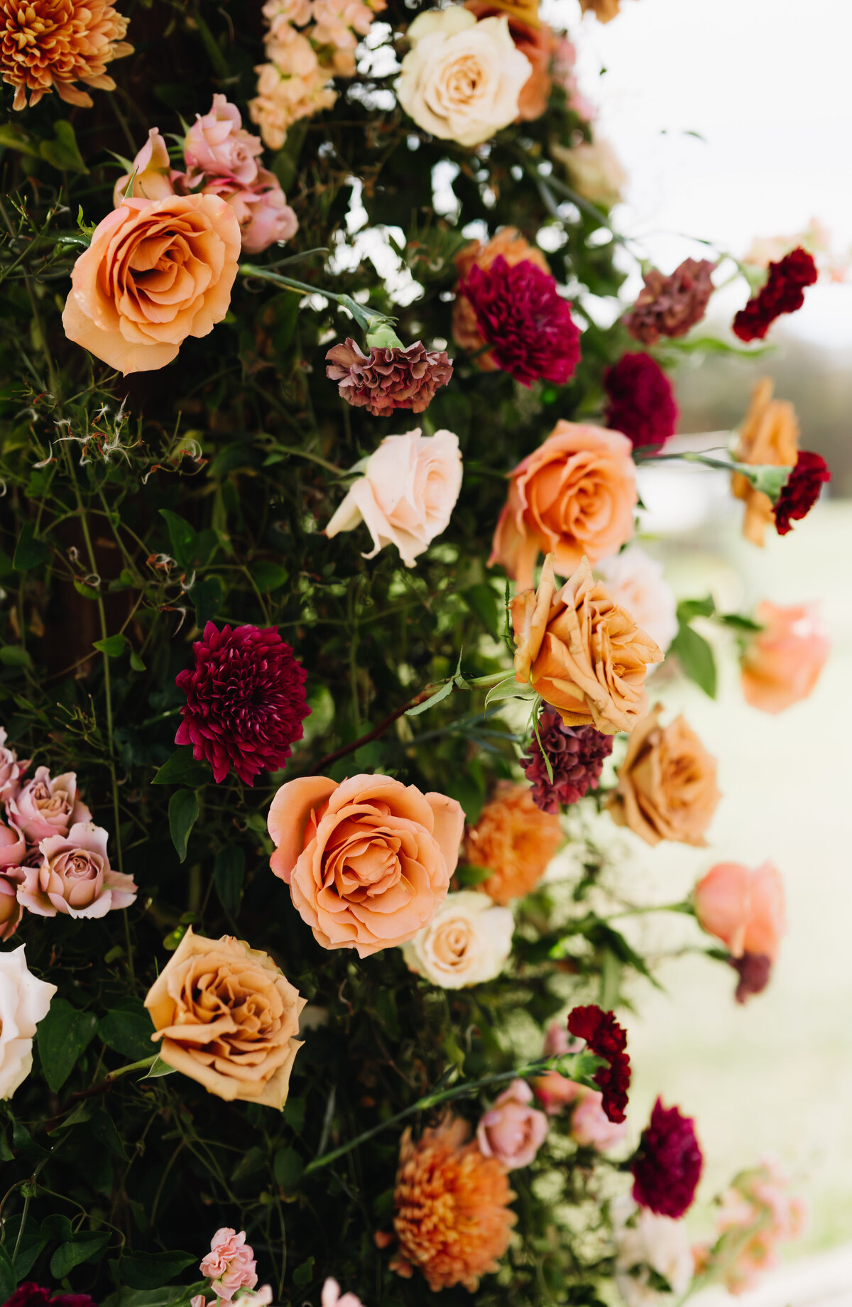 warm tone wedding florals in an arrangement at Charlottesville wedding venues ceremony space with mostly greenery and touches of orange and red flowers captured by Virginia wedding photographer