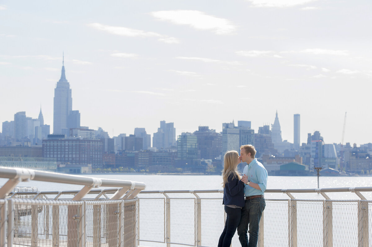 A couple kissing while standing next to a river overlooking a city 