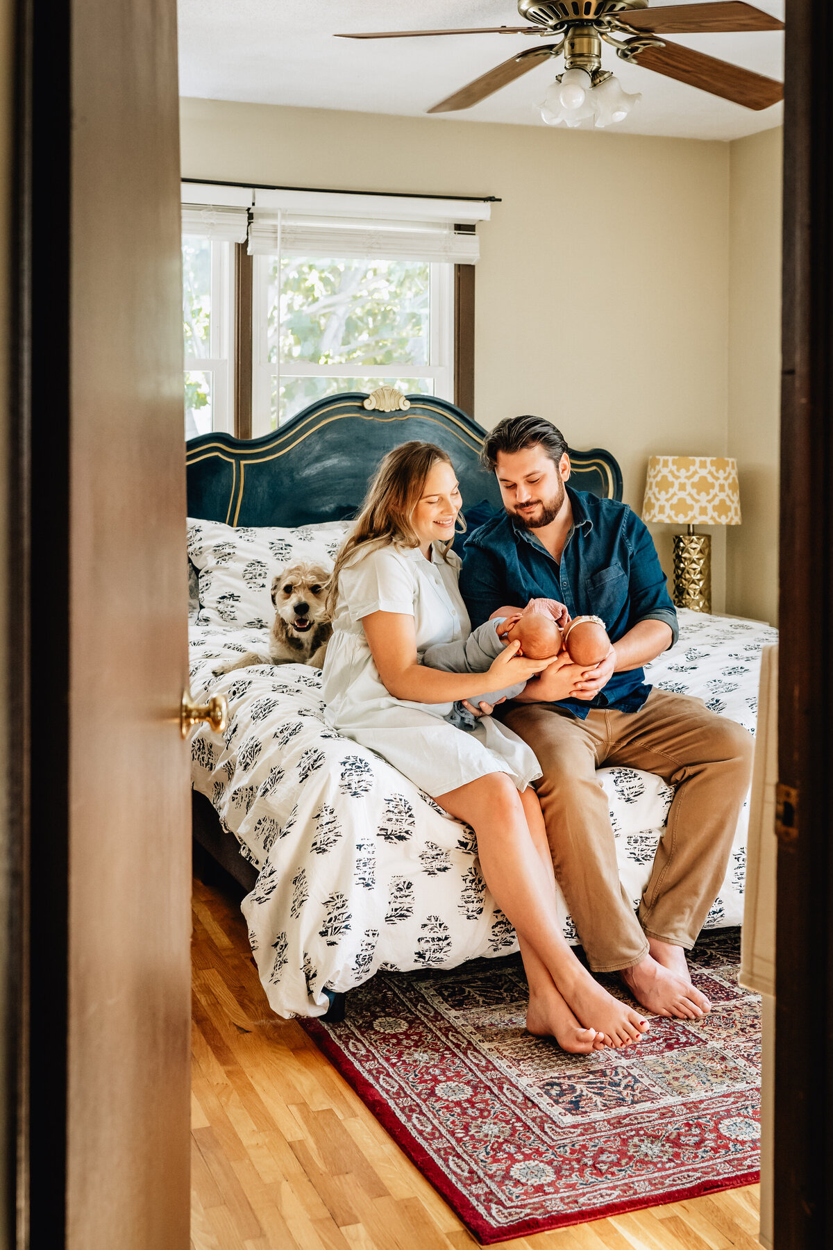 A cozy scene in a bedroom with a couple sitting on the bed, each holding one of their newborn twins.