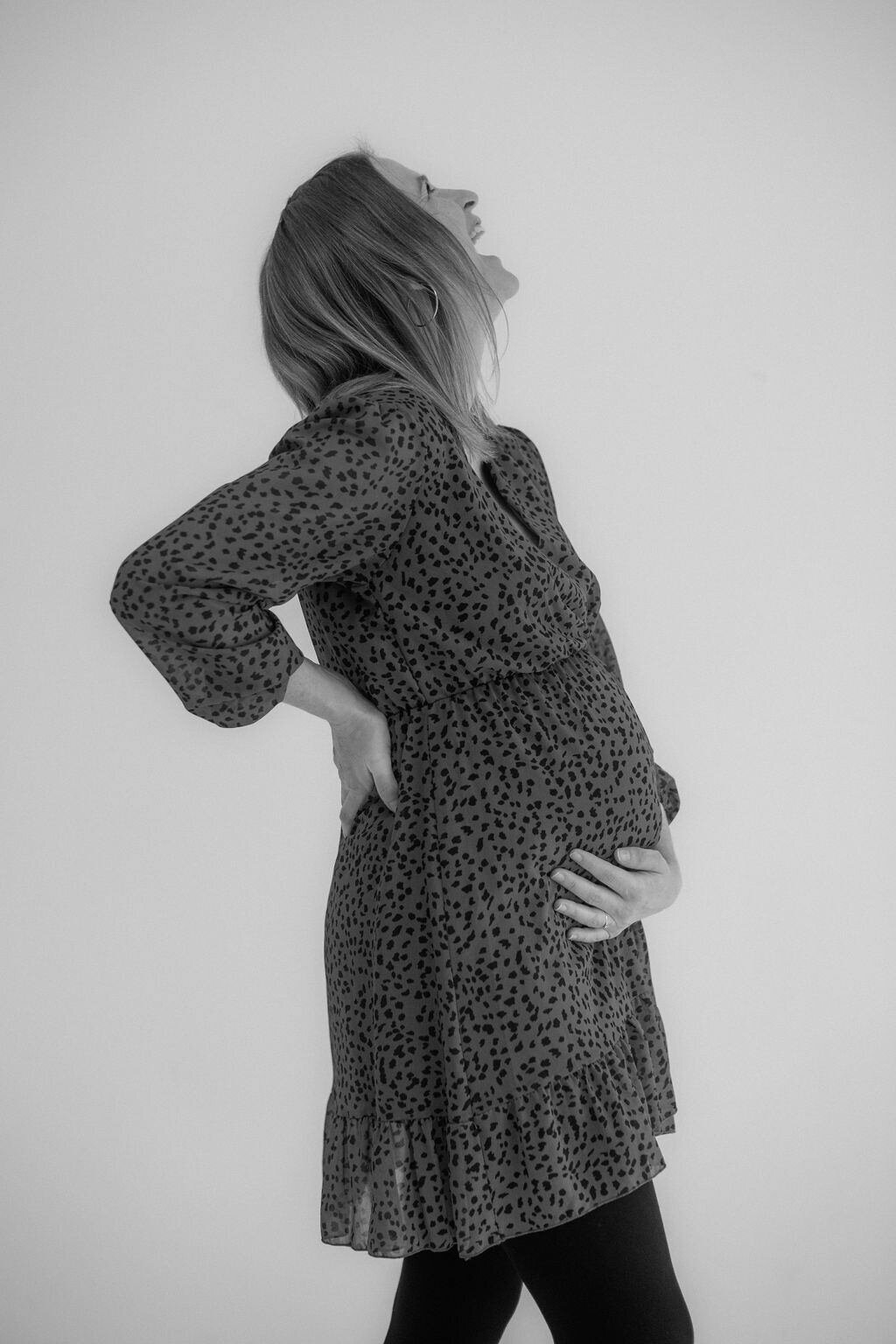 Pregnant woman laughing while holding her baby bump.