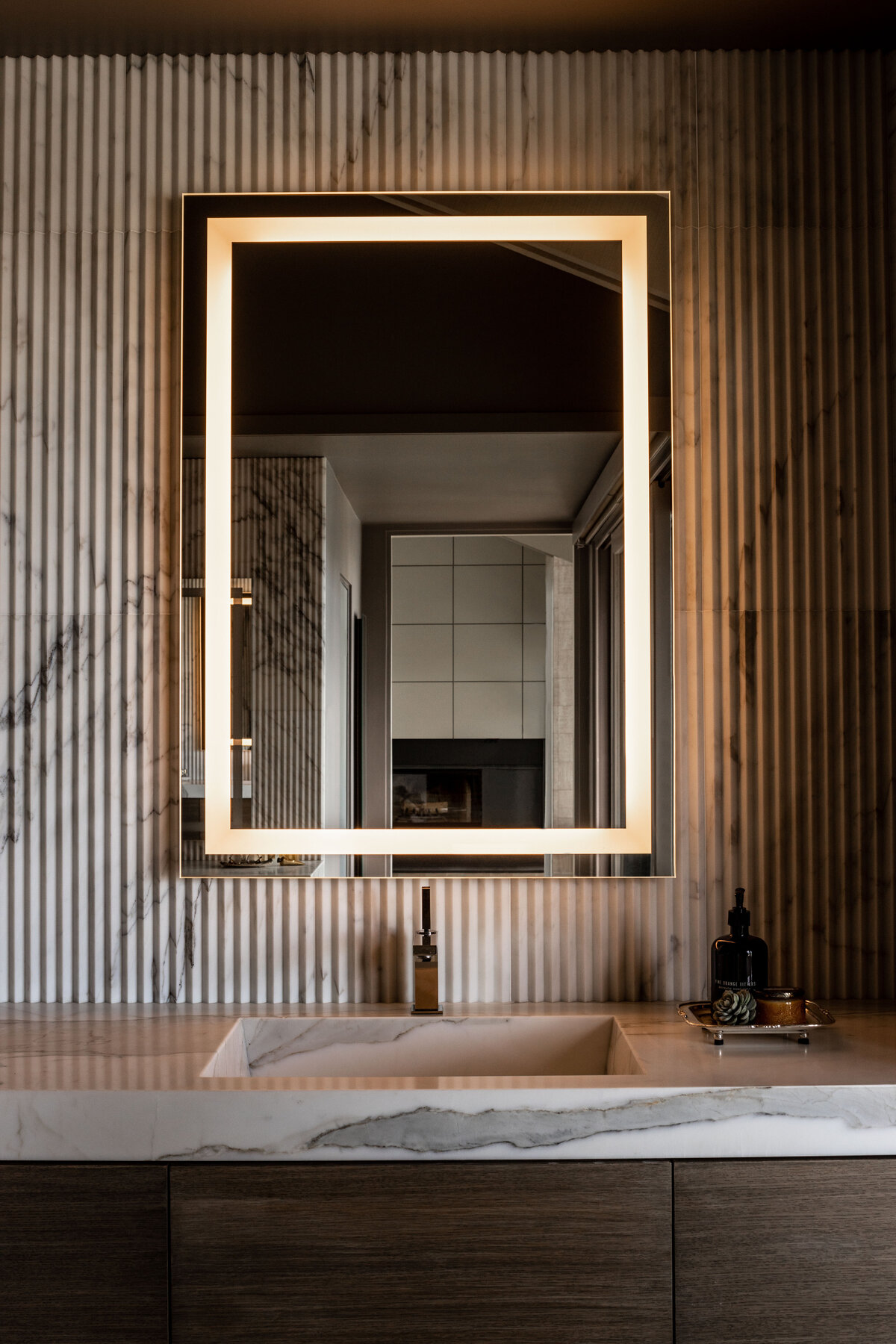 Luxurious bathroom with illuminated mirror and marble sink, featured in interior photography