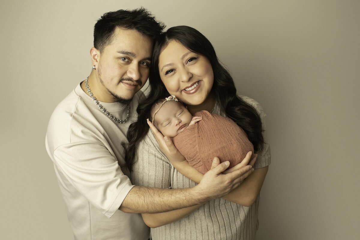 Mom and dad lovingly hold their newborn baby while smiling at the camera, capturing a joyful and heartwarming family moment