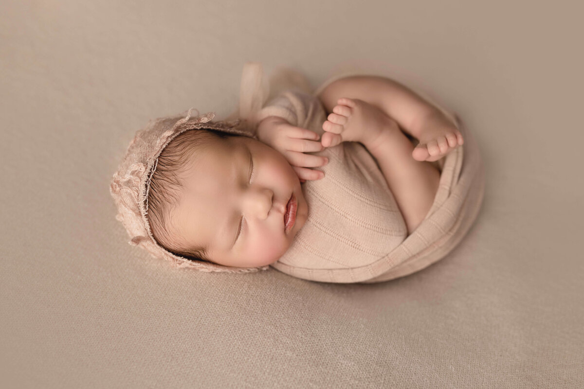 Newborn girl swaddled on ivory blanket with bonnet