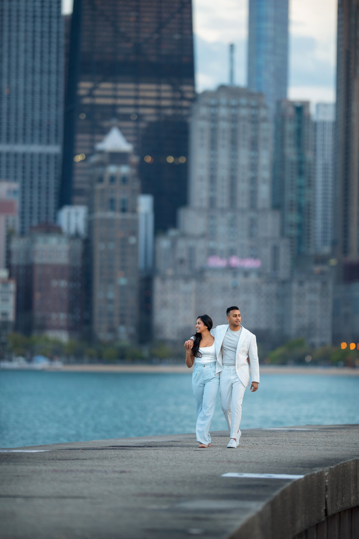 Stylish Indian fiancé and fiancée walking and looking at Lake Michigan and Chicago skyscrapers at North Ave Beach