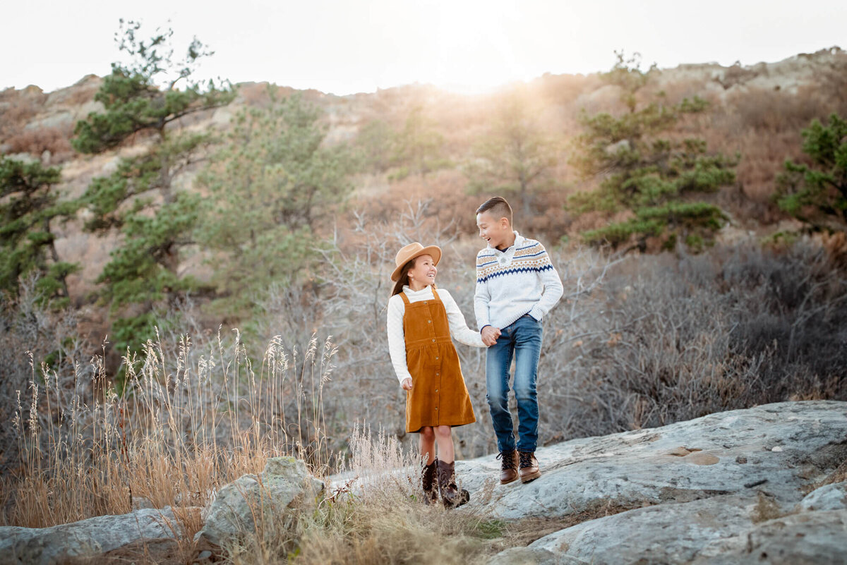 A young boy walks with his sister on a rock hand in hand at sunset