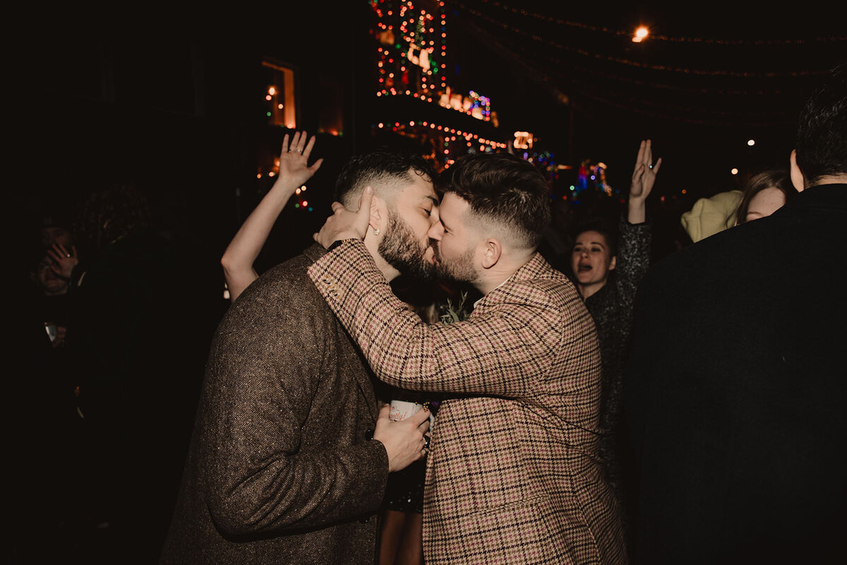 A wedding couple kissing with their guests cheering behind them 