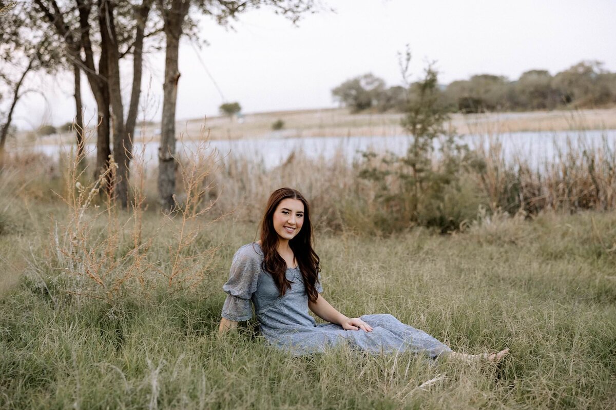 A senior girl is sitting in a grass field in Lubbock Texas.