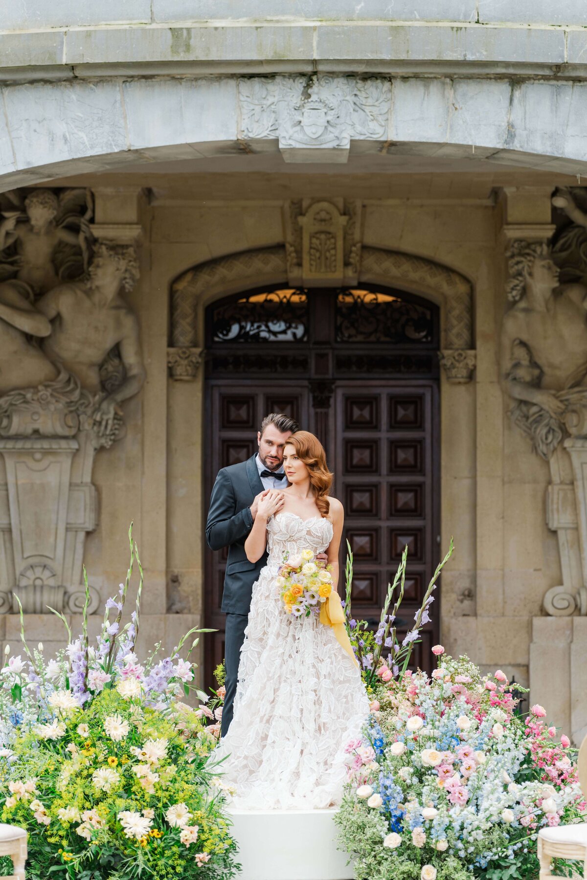 a bride and a groom stanting onn the Château Bouffémont , surounded by bbeautiful flowers