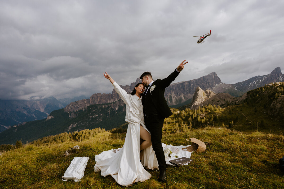 Couple celebrating on mountain meadow with arms raised.